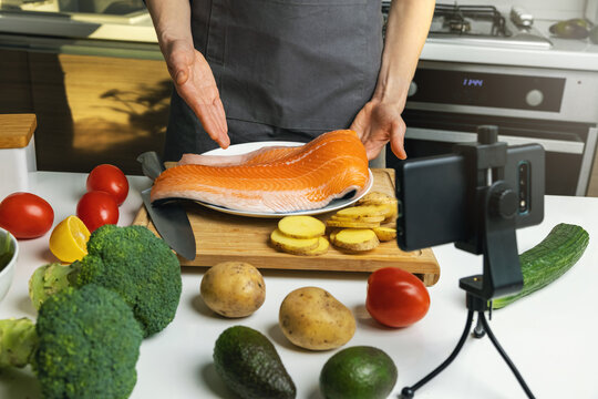food blogger recording video at home kitchen with phone. showing salmon preparing recipe - Powered by Adobe