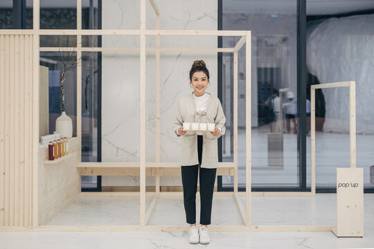 Beautiful asian woman standing in front of tea shop in uniform and giving away samples of drink tea for people to try tasting