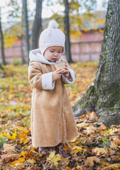 Beautiful baby in a coat drinking tea in the autumn forest