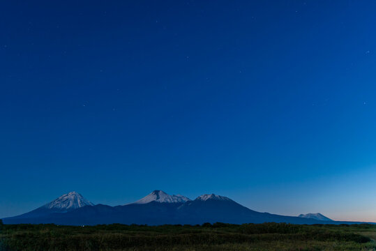 Night landscape with volcanoes peaks on a blue clear sky background, Kamchatka.