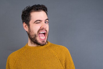 Fototapeta premium Young handsome Caucasian man wearing yellow sweater against gray wall winking looking at the camera with sexy expression, cheerful and happy face.
