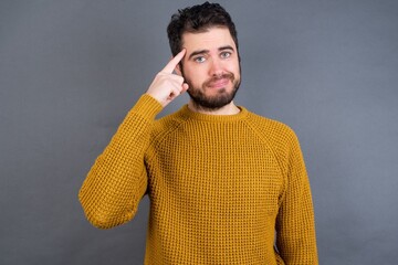 Young handsome Caucasian man wearing yellow sweater against gray wall tries to memorize something,...