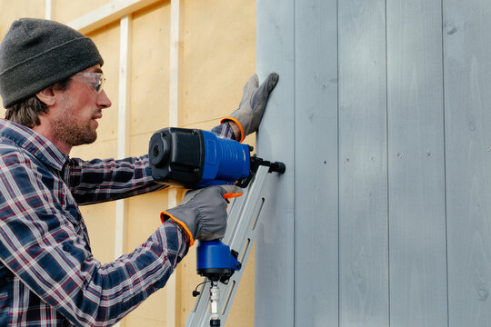Man with nail gun installing siding on house