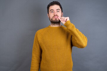Young handsome Caucasian man wearing yellow sweater against gray wall mouth and lips shut as zip...
