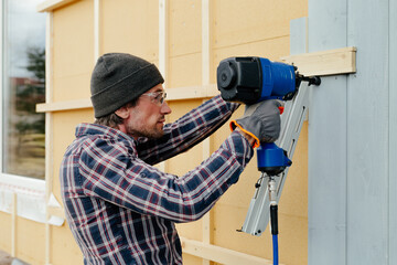 Man with nail gun installing siding on house