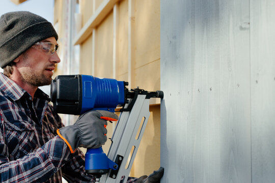 Man with nail gun installing siding on house
