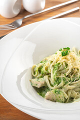 Tagliatelle pasta with pesto, chicken and Parmesan in a white plate on a wooden table, close up