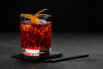 Classic Negroni Cocktail in a retro glass with ice and orange peel on a black background, space for...