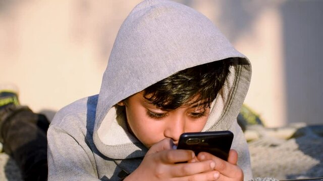 Portrait of little Indian boy using mobile phone indoor. Concept of mobile phone, technology addiction in young children.