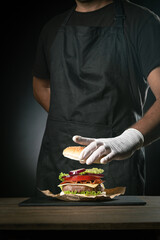 Chef preparing a hamburger on  dark background.