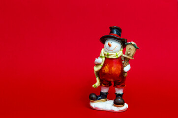 a toy snowman in a red suit and a black hat and a yellow scarf stands on a bright red background against a white background. new year or christmas card with place for text