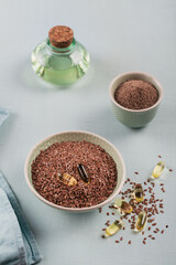Brown flax seed or linseed and ground or crushed flaxseed in small bowl and gelatin capsules with omega oil on a light blue background.