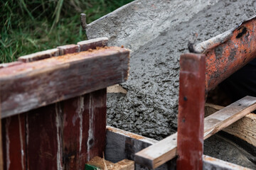 The concrete mixer unloads the concrete through a chute into a timber formwork with metal...