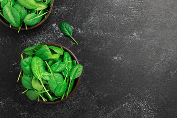 Fresh organic baby spinach leaves in the bowl on black rustic background top view. Healthy food...
