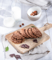 homemade chocolate cookies with chocolate chips, nuts, mint  and glass of milk  on a light morning wooden  table