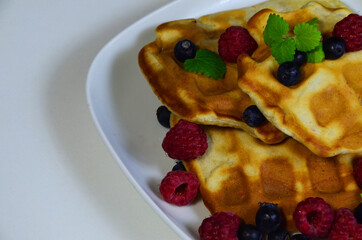 Homemade Belgium Waffles with fresh blueberries for breakfast. White plate, Viennese waffles with raspberries and mint. quick delicious breakfast on white background. top view copy space