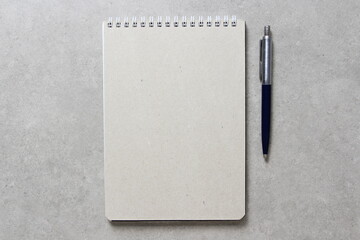 A spring notebook with a sheet of craft paper A5 with a ballpoint pen on light grey concrete background. Concept of new idea, business plan and strategy. Empty space for text