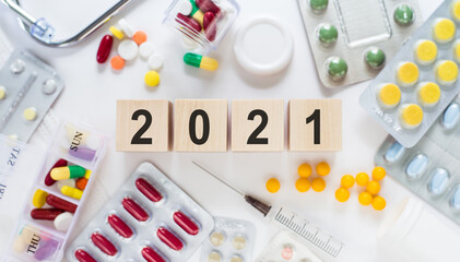 2021 text on wooden blocks on a desk. Medical concept with pills, vitamins, stethoscope and syringe on the background.