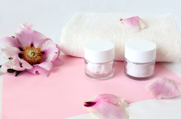 White Terry towel with delicate peony flower and body care creams, side view, space for text - the concept of gentle body care