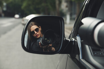 Private detective with camera spying from auto, view through car side mirror