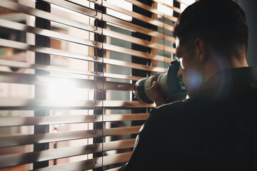 Private detective with camera spying near window indoors - obrazy, fototapety, plakaty