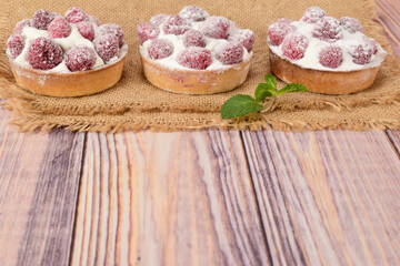 Side view of raspberry tartlets lying on a matting on a wooden table.