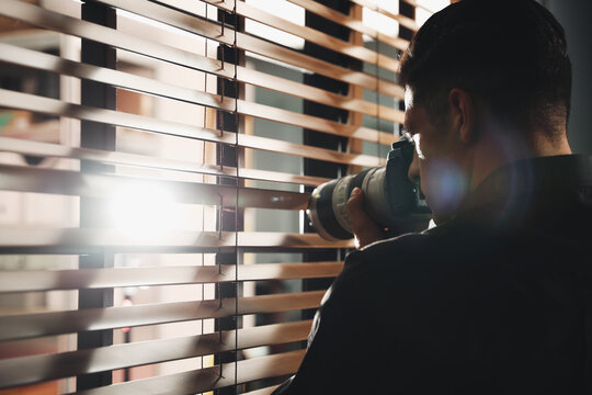 Private detective with camera spying near window indoors