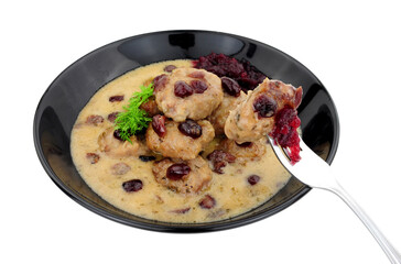 Swedish style meatballs in a creamy sauce with cranberries and cranberry sauce in a black bowl isolated on a white background