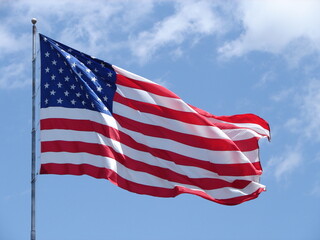 American flag, United States of America flag, waving in the wind, with blue sky and light clouds, red white and blue