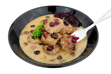 Swedish style meatballs in a creamy sauce with cranberries and cranberry sauce in a black bowl isolated on a white background