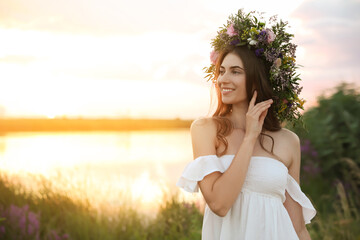 Fototapeta na wymiar Young woman wearing wreath made of beautiful flowers outdoors at sunset