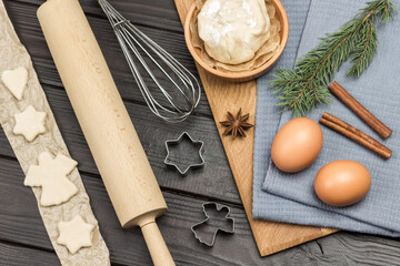 Eggs, Dough, cinnamon sticks and spruce twigs on gray napkin. Cutting shaped cookies by mold, molds, rolling pin and whisk
