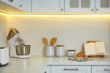 Countertop with modern food processor, cookbook and fresh bread in stylish kitchen