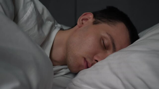 Calm handsome man goes to sleep in comfortable cozy fresh bed enjoying healthy good sleep nap.
