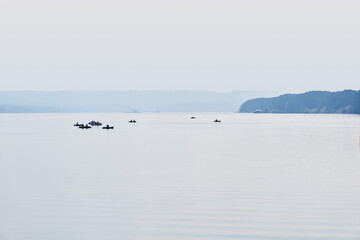 fishermen in inflatable boats fish on a wide river in the morning fog