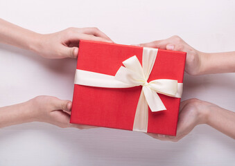 Top view of male and female hands holding red gift box with white ribbon on white background. Present for birthday, valentine day, Christmas, New Year. Congratulations background copy space.