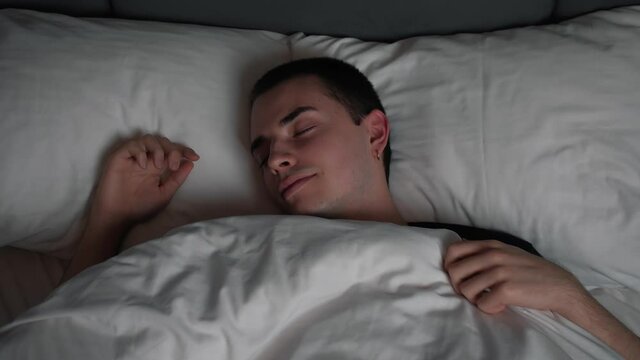 Calm smiling handsome man goes to sleep in comfortable cozy fresh bed enjoying healthy good sleep nap.