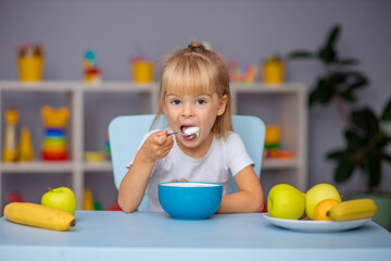 little girl eats porridge or cottage cheese for breakfast