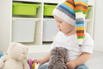 baby toddler boy in funny hat playing with teddy bear at home. Developing games for children.