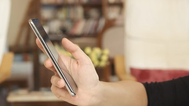 Smartphone. Young adult hand holding and using mobile phone technology device indoors side view 4K.