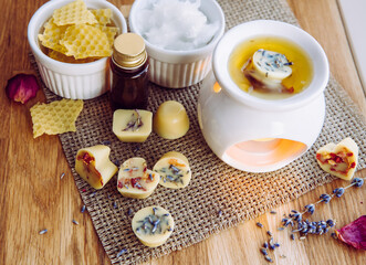 Using homemade mini wax melts in aromatherapy lamp diffuser at home interior concept. Melts making ingredients on table for unbleached beeswax, solid coconut oil, essential oil, dried flowers.