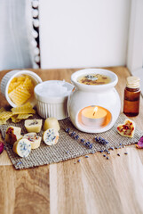 Using homemade mini wax melts in aromatherapy lamp diffuser at home interior concept. Melts making ingredients on table for unbleached beeswax, solid coconut oil, essential oil, dried flowers.