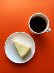 cup of coffee and a cake,  a cup of coffee and a piece of cheesecake on an orange table, top view