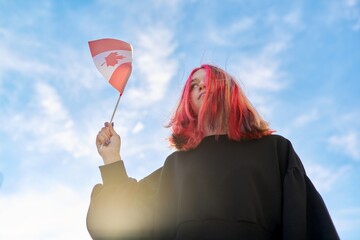 Student girl teenager with Canada flag in hand, blue sky with clouds background.