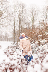 A young girl sits on a bench in a snowy park. It snows in winter. Girl in winter clothes in a snowy forest