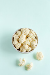 Cauliflower slices in a light bowl flat lay on a blue background with copy space.