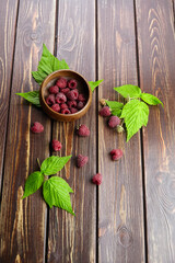 Fresh raspberry red berries with green leaves in bowl on wooden table