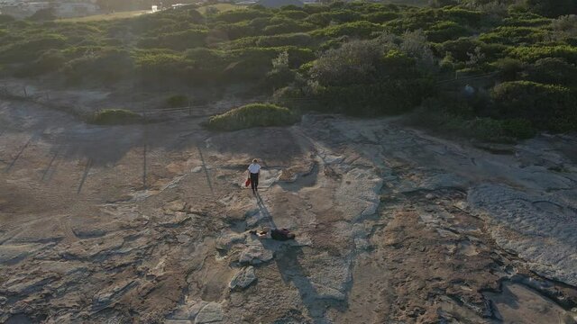 Man With Injured Knee Lying On Clovelly Cliffs Waiting For Ambulance Officer Assistance - Medic Check The Injured Tourist - Sydney, NSW, Australia. - Aerial