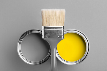 Two cans of yellow and gray paint with gray brush on gray background. Top view, repair concept.