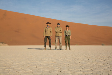 Three tourists in hakki clothes stand in the middle of Dead Vlei against the backdrop of a dune and...